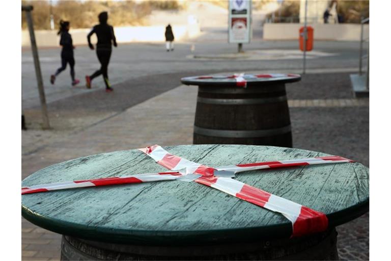 Kein gemütliches Beisammensein: Mit einem rot-weißen-Flatterband sind Stehtische an der Promenade des Ostseebades Warnemünde abgeklebt. Foto: Bernd Wüstneck/dpa-Zentralbild/dpa