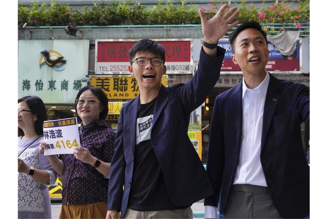 Kelvin Lam (r), demokratischer Kandidat für die Bezirkswahl, und der prodemokratische Aktivist Joshua Wong (M) winken Unterstützern zu. Foto: Vincent Yu/AP/dpa