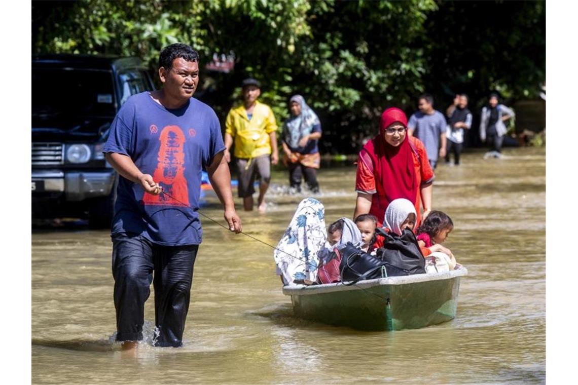 Malaysia: Tote und Vermisste bei Überschwemmungen Khairul Anuar Muhamad (l) zieht mit seiner Frau seine Kinder durchs Wasser, nachdem ihr Haus überflutet wurde. Foto: Zulkarnain Kamaruddin/BERNAMA/dpa