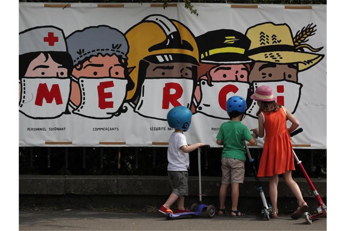 Kinder in Paris betrachten ein Banner, auf dem eine Danksagung an verschiedene systemrelevante Berufsgruppen aufgedruckt ist. Foto: Francois Mori/AP/dpa