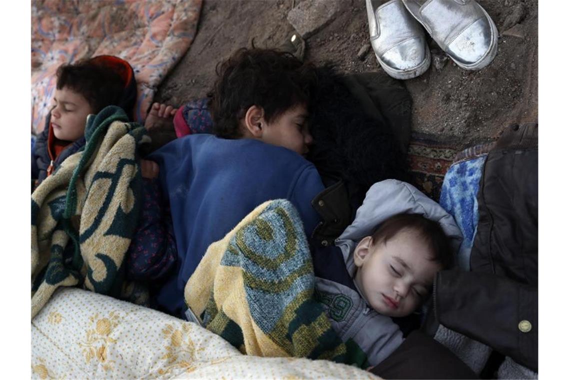 Kinder liegen schlafend auf dem Boden am Ufer des Flusses nahe der türkisch-griechischen Grenze. Foto: Darko Bandic/AP/dpa