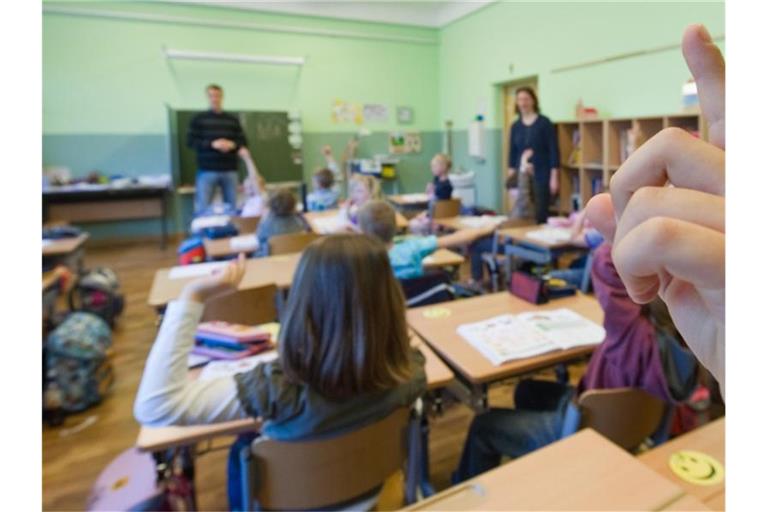 Kinder melden sich während des Unterrichts. Vor ihnen stehen zwei erwachsene Personen. Foto: Patrick Pleul/Archiv