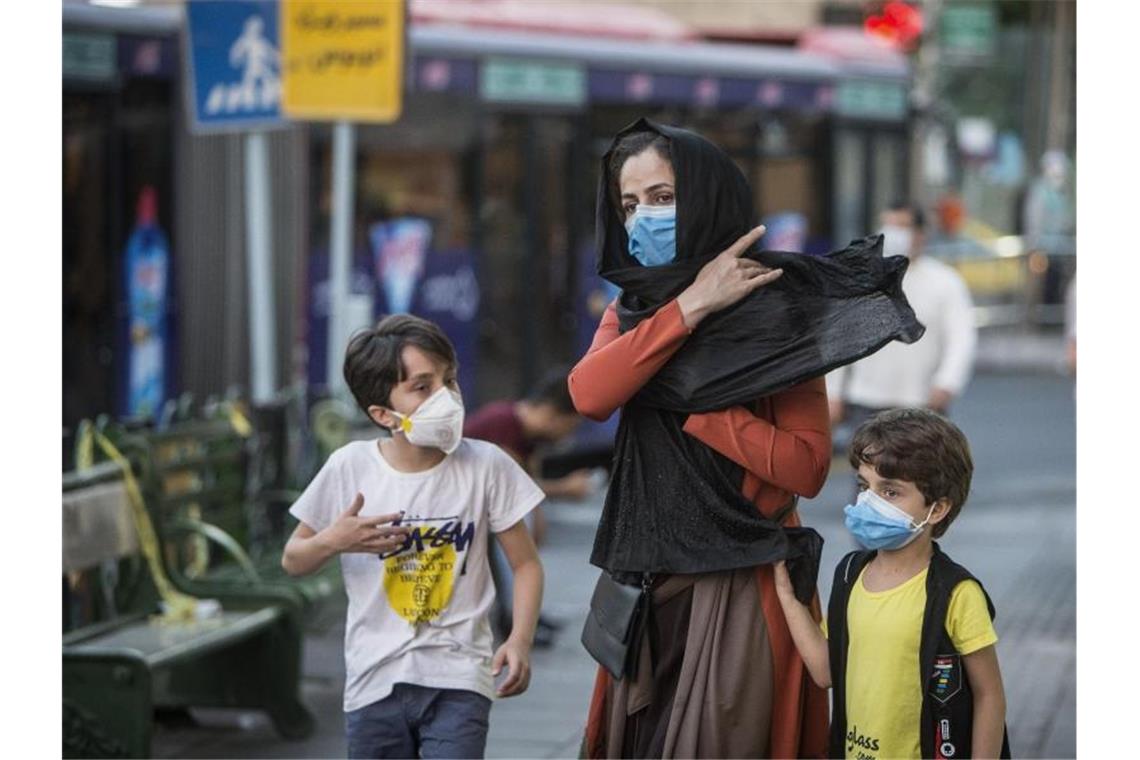 Irans Atomchef hat Corona - Fallzahlen steigen stark Kinder mit Gesichtsmasken gehen mit ihrer Mutter eine Straße entlang in Teheran. Der Iran hat nun Bußgelder bei Verstößen gegen die Corona-Regeln eingeführt. Foto: Ahmad Halabisaz/XinHua/dpa