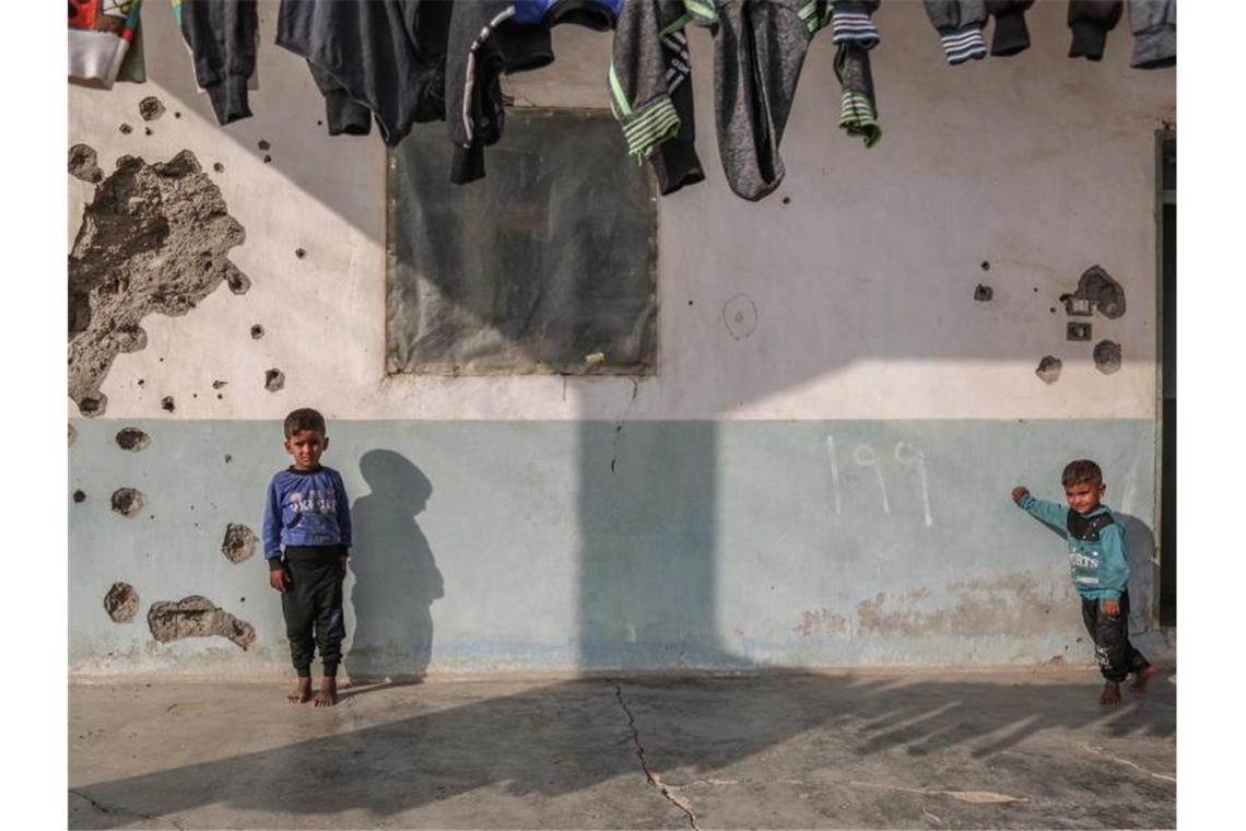 Kinder spielen vor einem Haus, dessen Wand durch Einschusslöcher beschädigt ist. Foto: Anas Alkharboutli/dpa