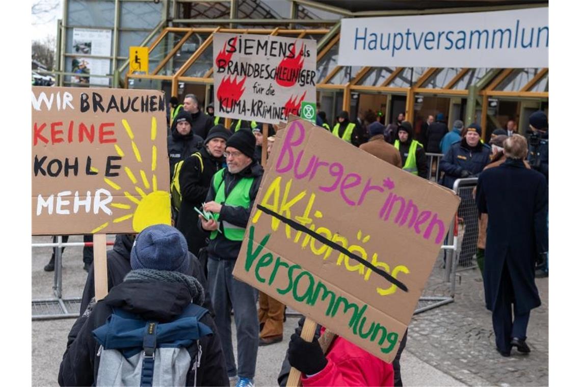 Klimaaktivisten demonstrieren mit Plakaten vor der Olympiahalle in München, wo die Siemens-Hauptversammlung stattfindet. Foto: Peter Kneffel/dpa