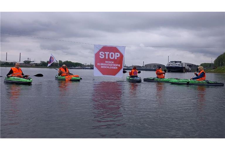 Klimaaktivisten der „Letzten Generation“ in Warnwesten blockieren mit Kajaks die Kanalzufahrt zum Ölhafen.