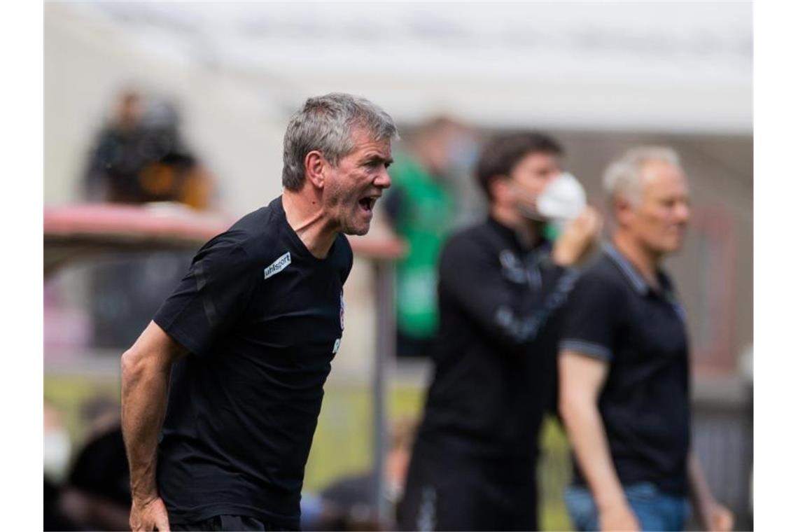 Kölns Trainer Friedhelm Funkel versucht seine Spieler auf dem Platz zu erreichen - im Hintergrund steht Freiburgs Trainer Christian Streich. Foto: Rolf Vennenbernd/dpa