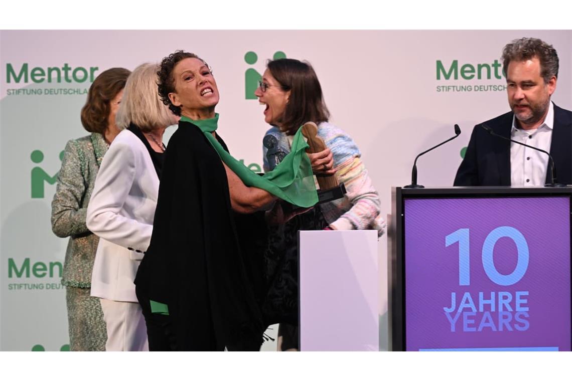 Königin Silvia von Schweden (l) und Bettina Gräfin Bernadotte (r) schauen zu, wie Sybille Perez (3.v.l), Leitung Mentor-Akademie, den Preis wieder aufhebt, der auf den Boden gefallen ist.