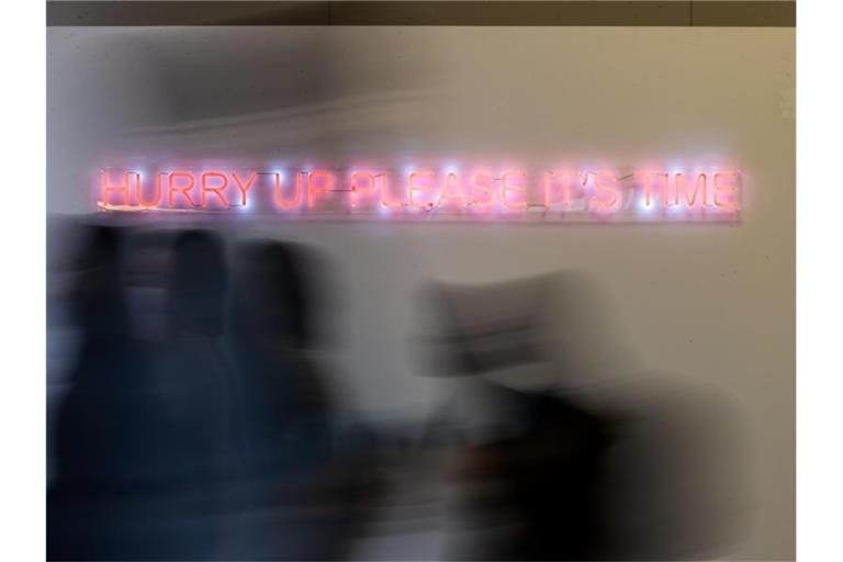 Konferenzteilnehmer gehen bei der UN-Klimakonferenz COP26 in Glasgow an einem Schriftzug der Künstlerin Cornelia Parker vorbei. Zu lesen ist „hurry up please it‘s time“ (beeilt euch, es ist Zeit). Foto: Christoph Soeder/dpa