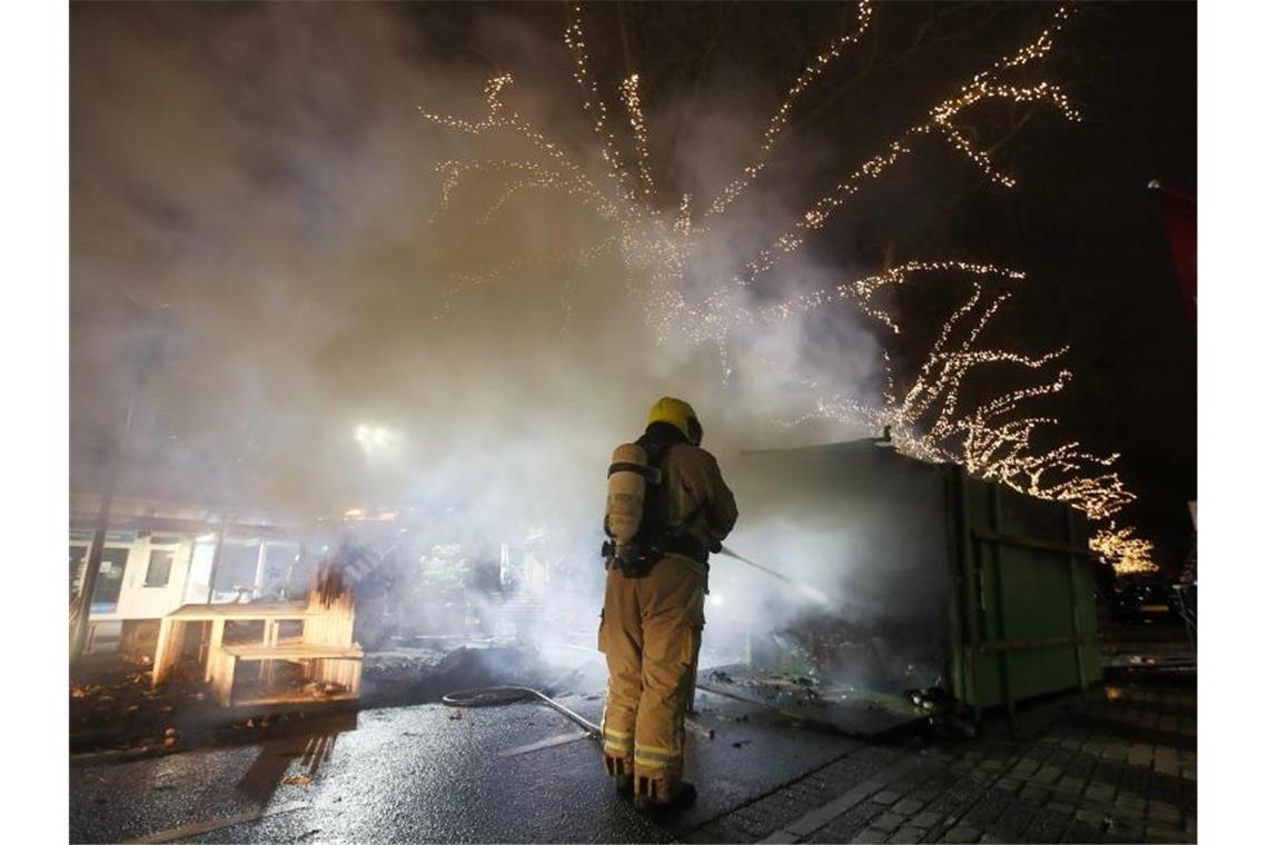 Krawalle in Rotterdam: Ein Feuerwehrmann löscht einen Container, der bei Protesten gegen die landesweite Ausgangssperre in Brand gesetzt wurde. Foto: Peter Dejong/AP/dpa