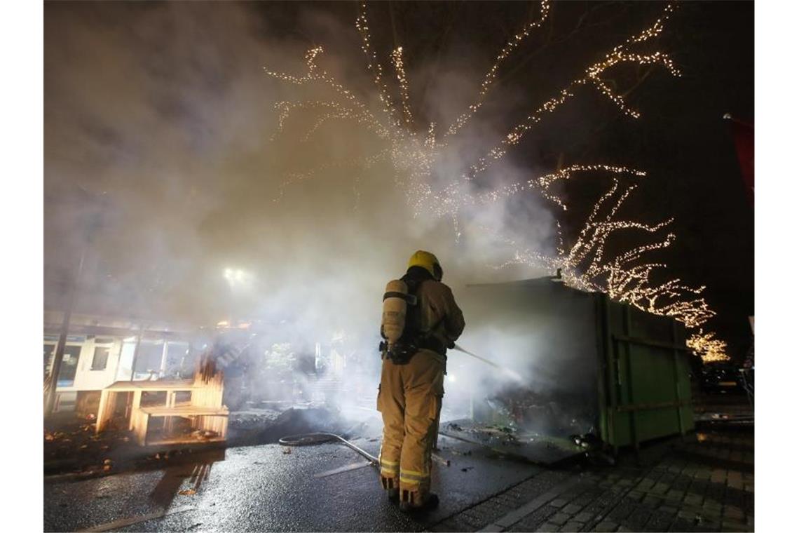 Corona-Krawalle schockieren Niederlande Krawalle in Rotterdam: Ein Feuerwehrmann löscht einen Container, der bei Protesten gegen die landesweite Ausgangssperre in Brand gesetzt wurde. Foto: Peter Dejong/AP/dpa