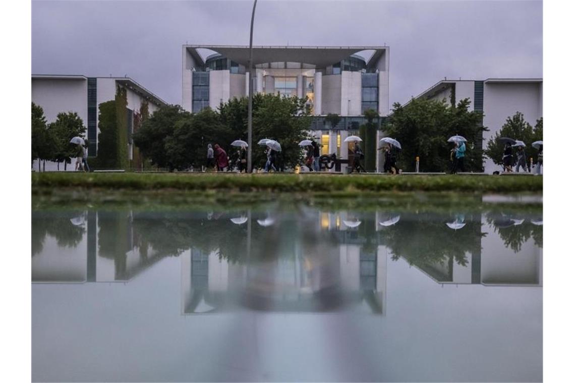 Kühl und grau: Eine Gruppe mit Regenschirmen geht am Bundeskanzleramt vorbei. Foto: Christoph Soeder