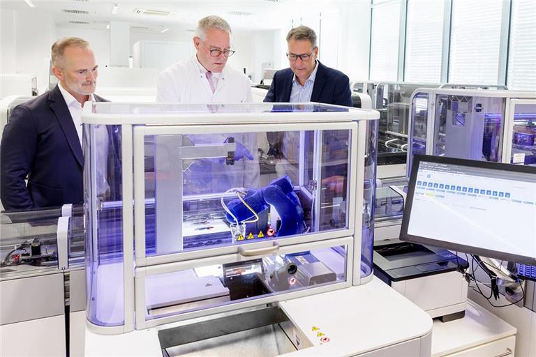 Landrat Richard Sigel (rechts) und Klinik-Geschäftsführer André Mertel (links) lassen sich von Chefarzt Hannes Wickert am Startmodul der Flexlab-X-Automation zeigen, wie der Roboterarm die Röhrchen greift und auf die Reise schickt.  Foto: RMK/Fuchs