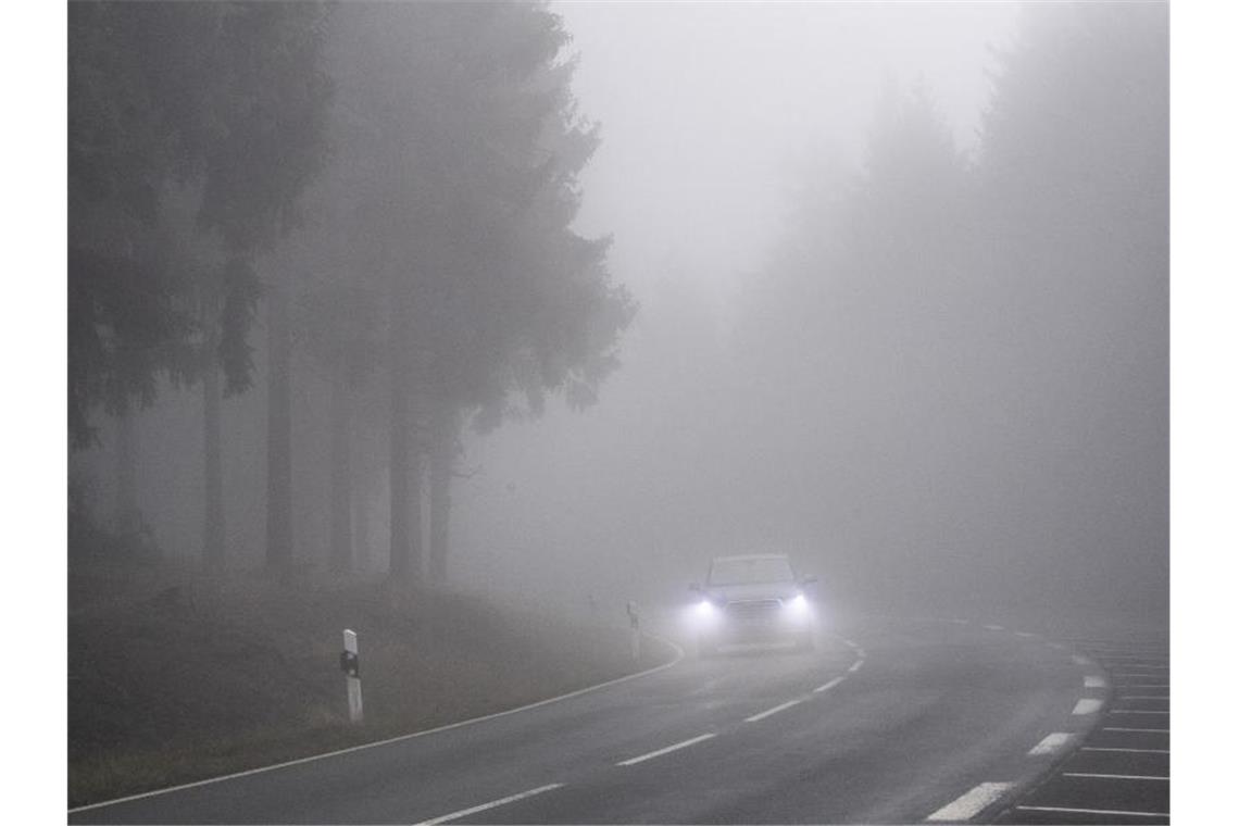 Langsam fährt ein Auto durch den dichten Nebel im Taunus. Foto: Boris Roessler/dpa