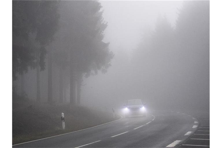 Langsam fährt ein Auto durch den dichten Nebel im Taunus. Foto: Boris Roessler/dpa