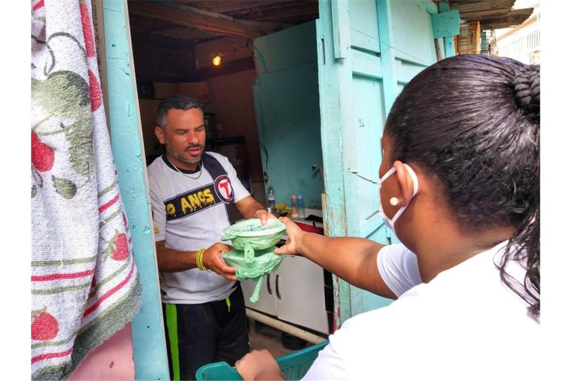 Laryssa da Silva reicht einem Mann zwei Essenspakete in die Wohnung. Sie ist eine von 700 "Straßenpräsidenten" in Paraisopolis. Foto: Caio Capicoré/G10 Favelas/Presidentes de Rua/dpa