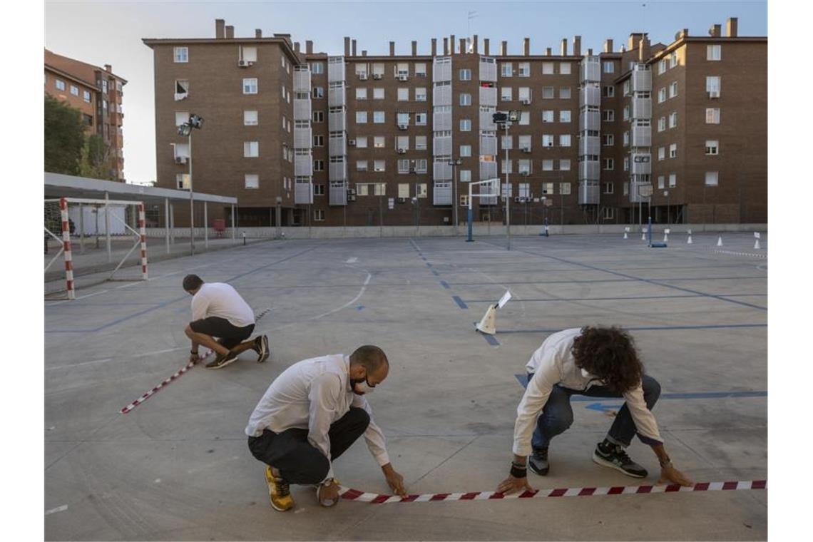 Lehrer machen mit Klebeband Markierungen auf einem Schulhof in Madrid, um den Sicherheitsabstand zwischen den Schülern zu gewährleisten. Foto: Bernat Armangue/AP/dpa