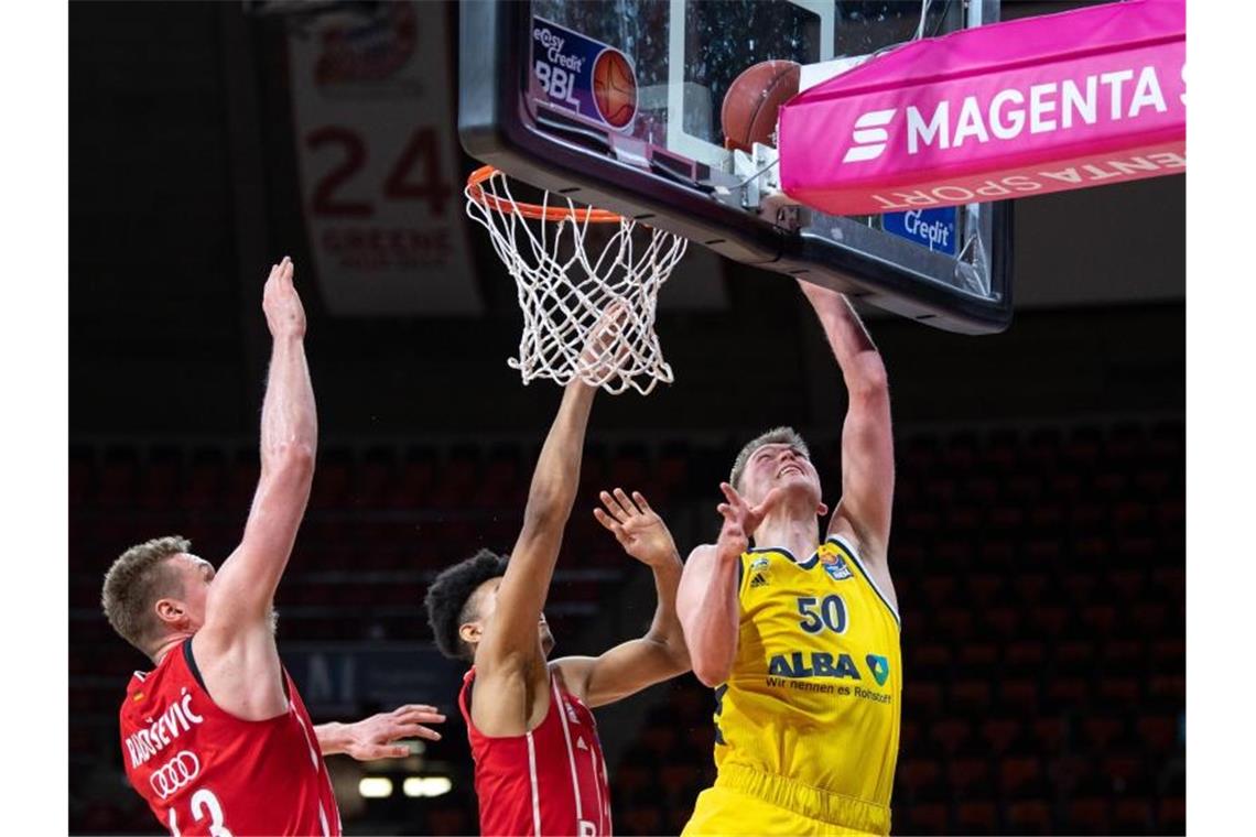 Leon Radosevic (l-r) und Jason George von Bayern München versucht Ben Lammers von Alba Berlin am Korb zu blocken. Foto: Matthias Balk/dpa