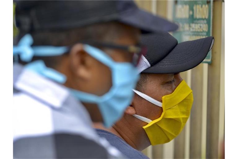 Männer mit Mundschutzmasken am Eingang des Friedhofs „Jardines de la Esperanza“ in der Hafenstadt Guayaquil in Ecuador. Foto: Marcos Pin Mendez/dpa