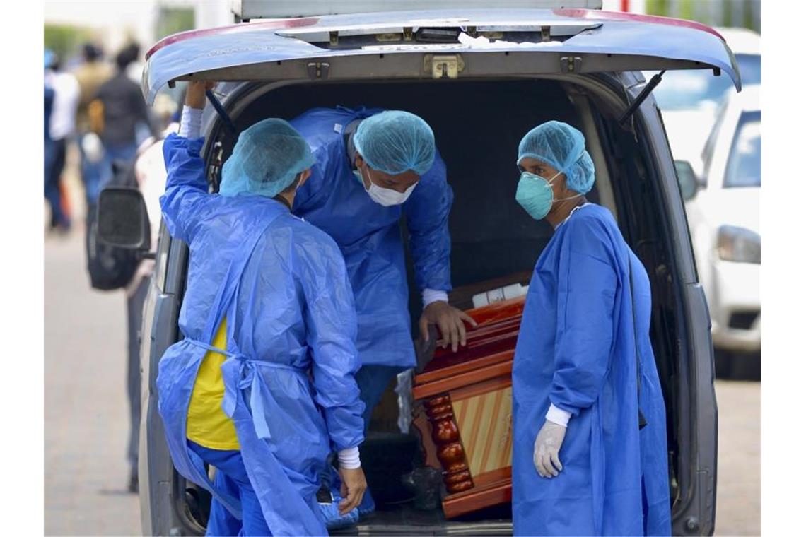 Männer mit Schutzanzügen laden in der Hafenstadt Guayaquil in Ecuador einen Sarg in einen Wagen vor einem Krankenhaus. Foto: Marcos Pin Mendez/dpa