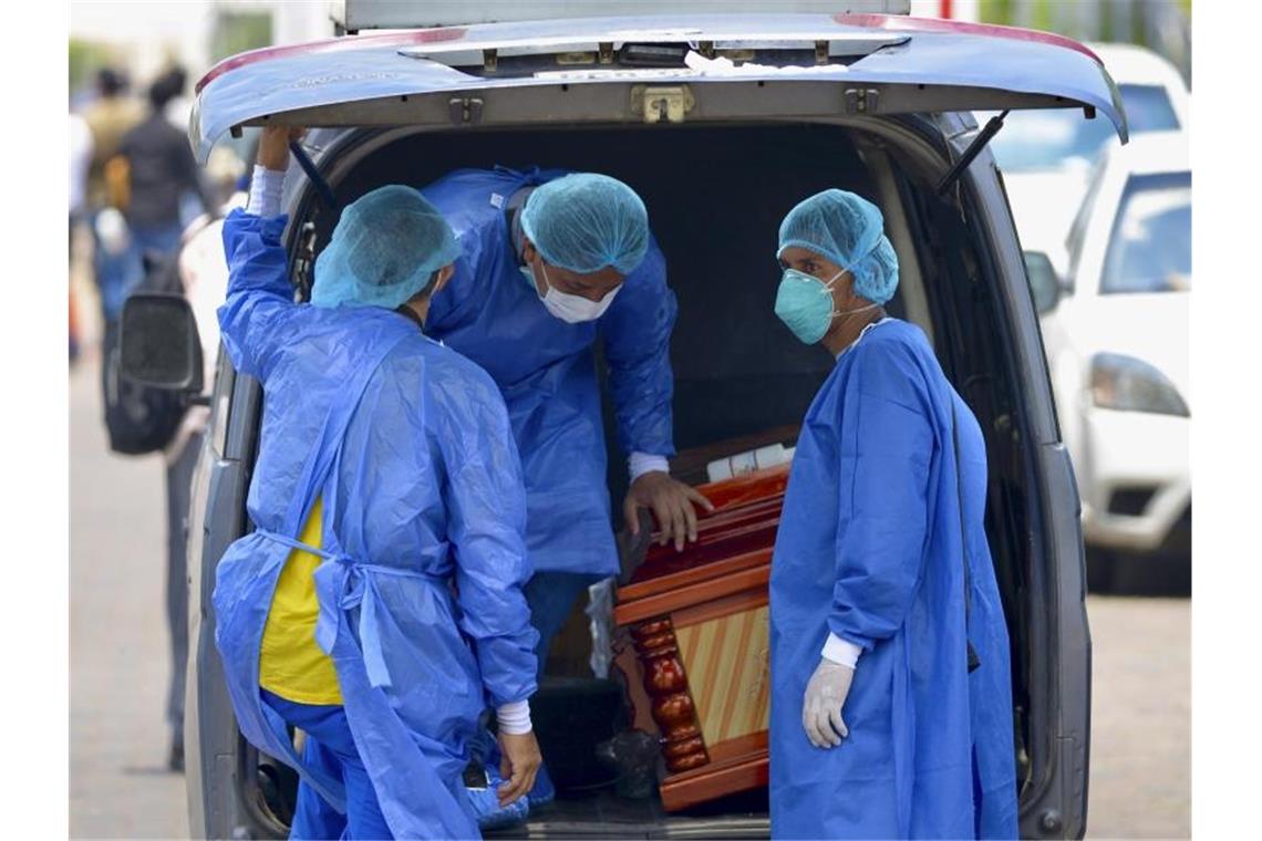 Männer mit Schutzanzügen laden vor einem Krankenhaus in Ecuador einen Sarg in einen Wagen. Foto: Marcos Pin Mendez/dpa/Archiv