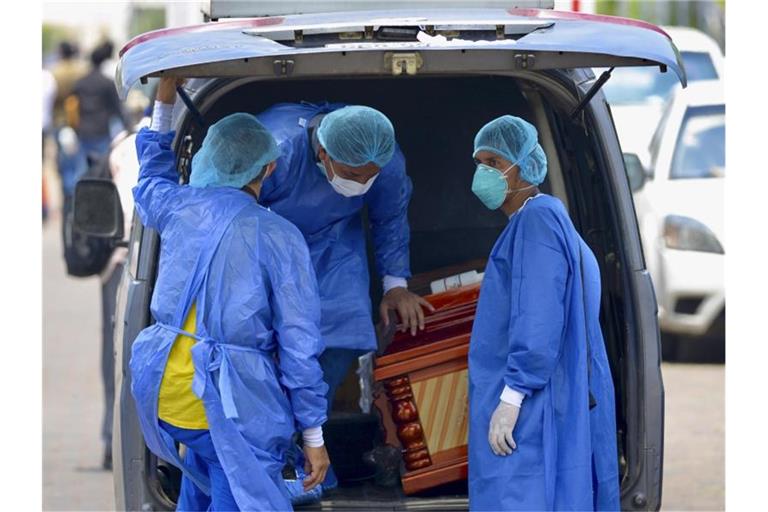 Männer mit Schutzanzügen laden vor einem Krankenhaus in Ecuador einen Sarg in einen Wagen. Foto: Marcos Pin Mendez/dpa/Archiv