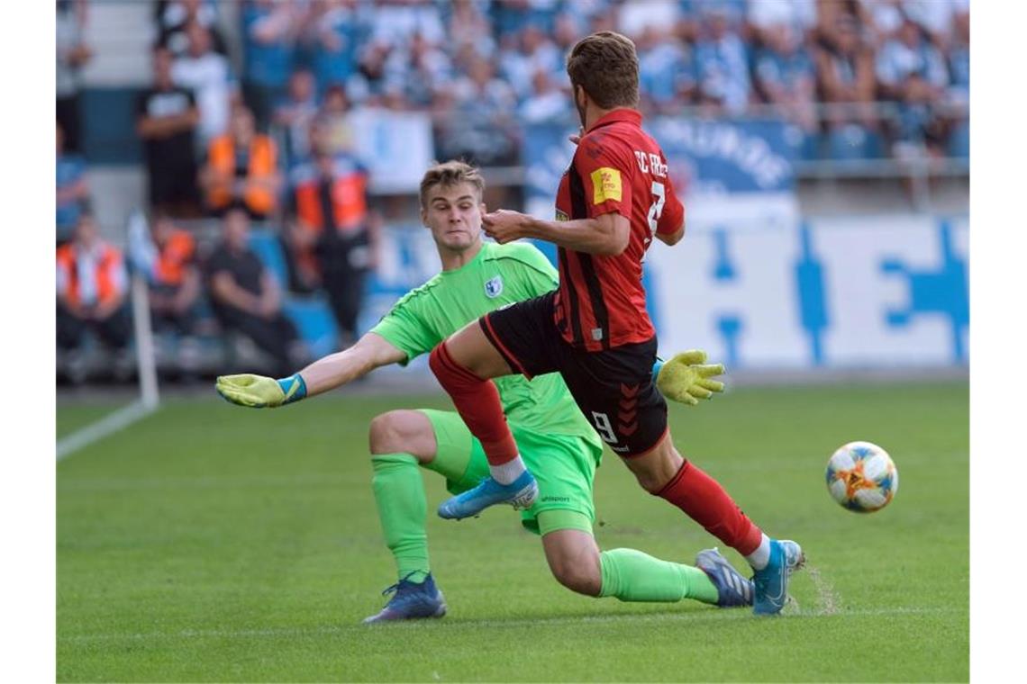 Freiburg zittert sich beim 1. FC Magdeburg weiter Magdeburgs Torwart Morten Behrens (l.) und Freiburgs Lucas Höler kämpfen um den Ball. Foto: Peter Steffen