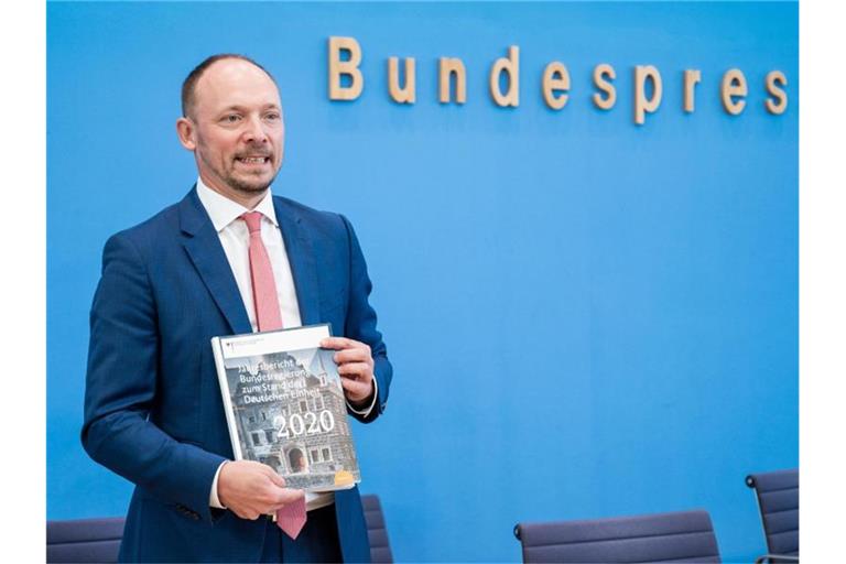 Marco Wanderwitz (CDU), Ostbeauftragter der Bundesregierung, zeigt bei der Vorstellung den Jahresbericht zum Stand der Deutschen Einheit 2020. Foto: Christophe Gateau/dpa