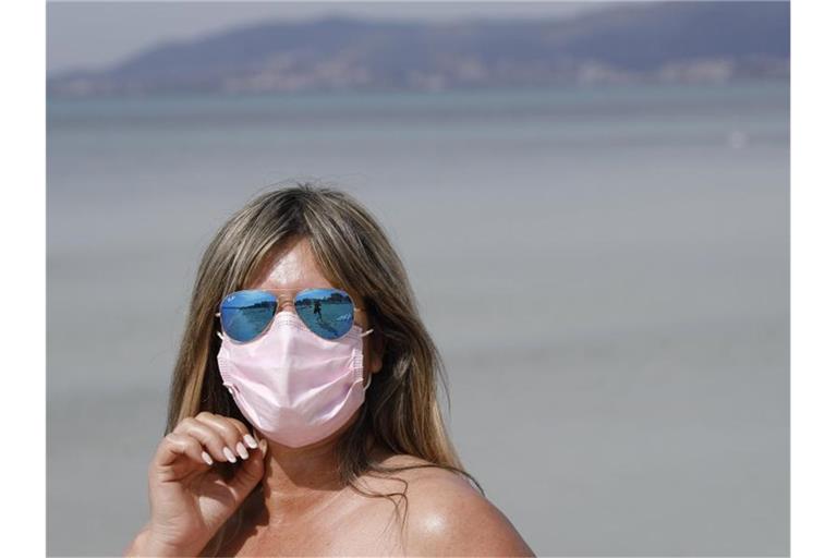 Maske am Strand: Auch 2021 steht der Sommerurlaub - wie hier auf Mallorca - ganz im Zeichen der Pandemie. Foto: Clara Margais/dpa