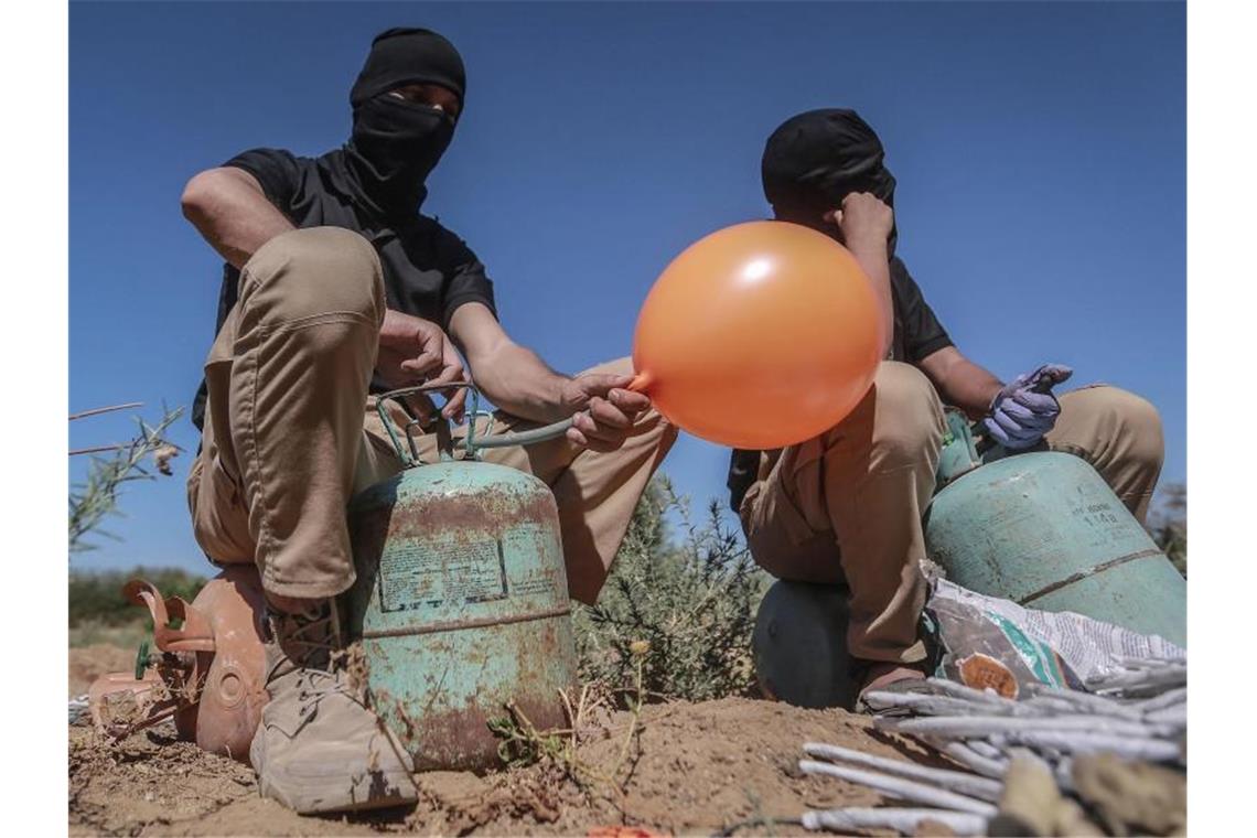 Maskierte Palästinenser präparieren Brandballons. Foto: Mohammed Talatene/dpa