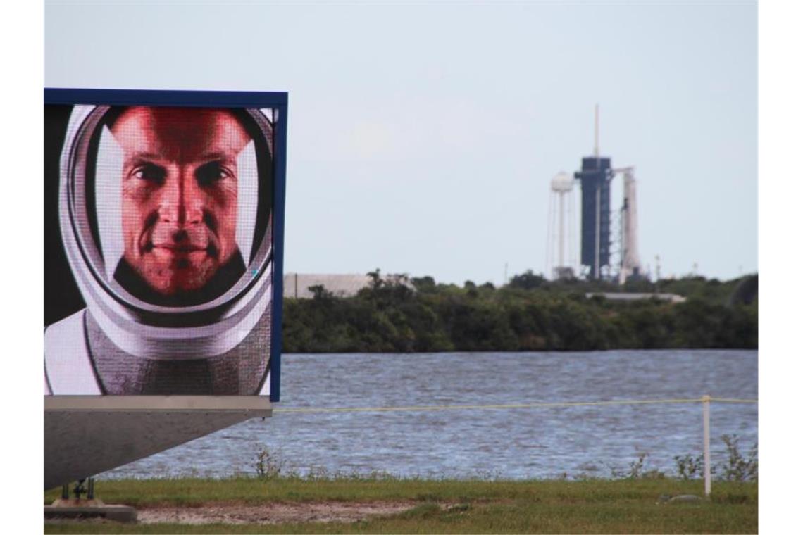 Matthias Maurer auf einem Video-Bildschirm vor dem Launchpad 39A in Cape Canaveral, an dem schon die Falcon-9-Rakete mit Crew Dragon-Kapsel aufgestellt ist. Foto: Christina Horsten/dpa
