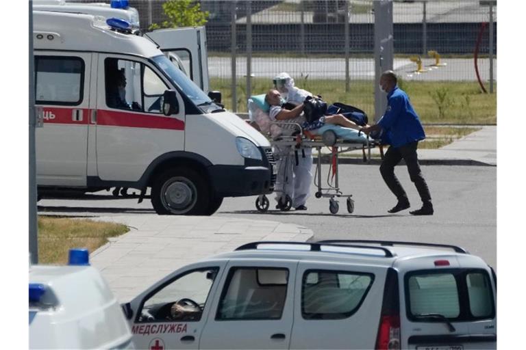Medizinische Mitarbeiter - einer mit einer speziellen Schutzausrüstung - begleiten einen Mann mit Verdacht auf Covid-19 zu einem Krankenhaus in Kommunarka bei Moskau. Foto: Pavel Golovkin/AP/dpa