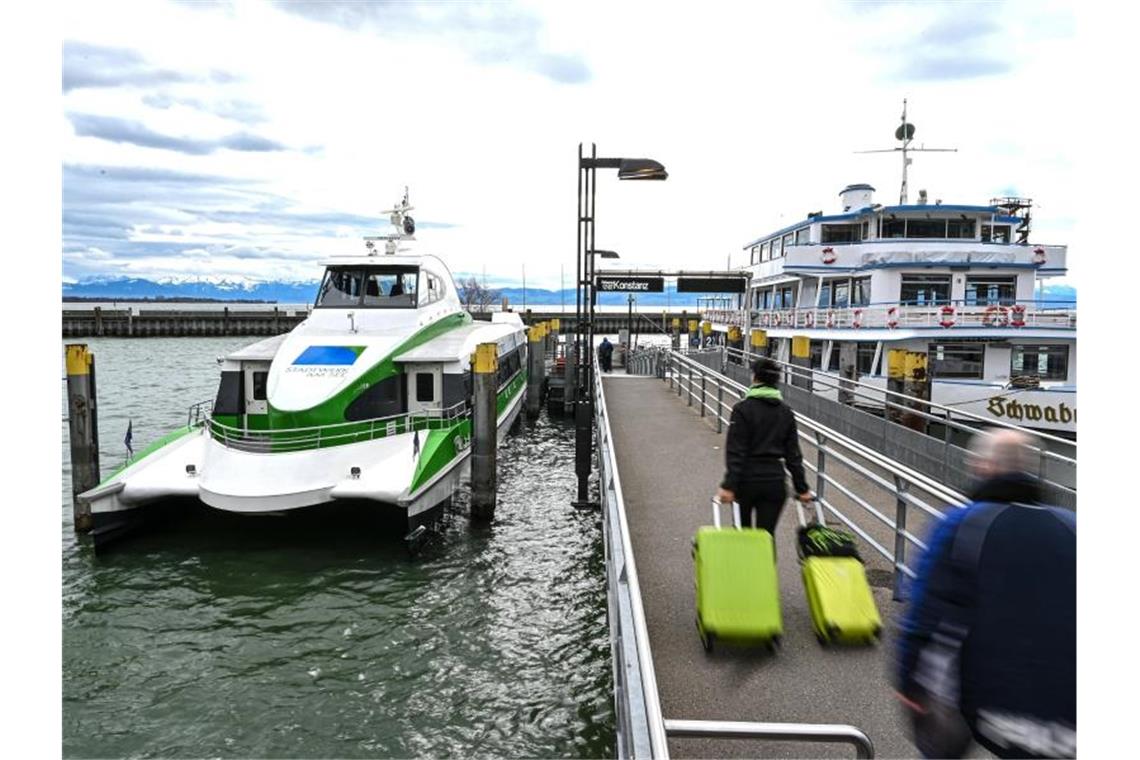 Mehrere Fußgänger laufen auf der Mole zum Katamaran, der auf dem Bodensee nach Konstanz fährt. Foto: Felix Kästle/dpa/Archivbild