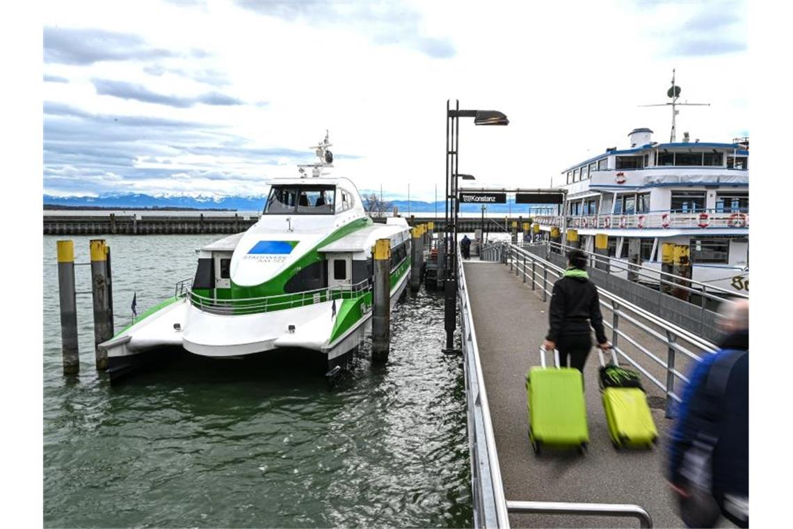 Mehrere Fußgänger laufen auf der Mole zum Katamaran, der auf dem Bodensee nach Konstanz fährt. Foto: Felix Kästle/dpa/Symbolbild