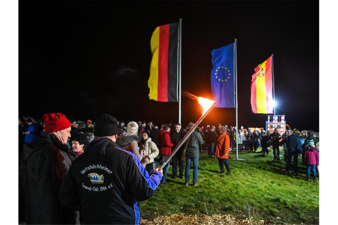 Mehrere hundert Menschen stehen in Gadheim unter den Flaggen Deutschlands, der Europäischen Union und Veitshöchheims. Foto: Nicolas Armer/dpa
