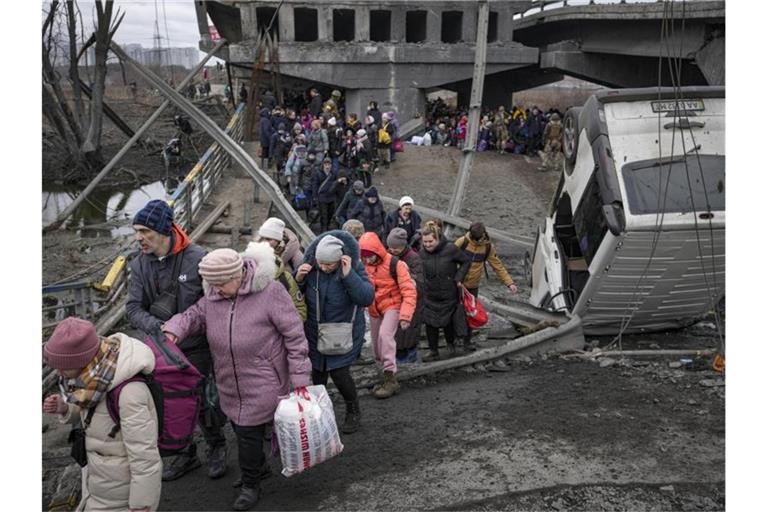 Menschen aus der Ukraine überqueren den Fluss Irpin auf einem improvisierten Weg unter einer zerstörten Brücke. Foto: Vadim Ghirda/AP/dpa
