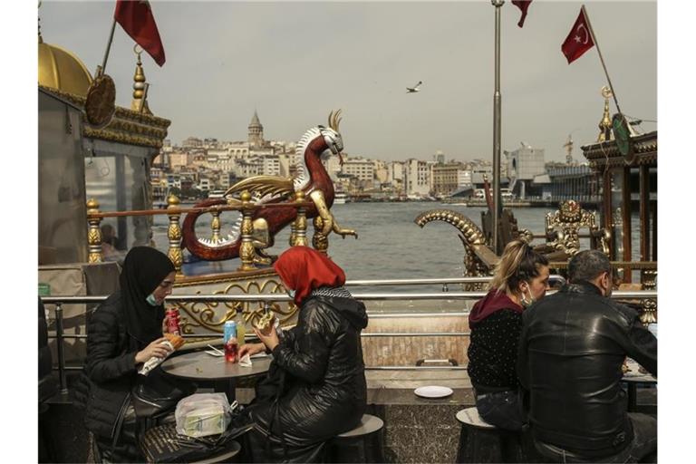 Menschen essen an Tischen am Ufer vom Goldenen Horn auf dem Eminonu Markt in Istanbul. Foto: Emrah Gurel/AP/dpa