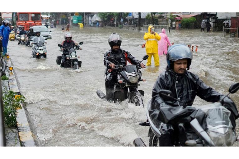 Menschen fahren bei starkem Regen in Mumbai mit Motorrädern durch eine überschwemmte Straße.