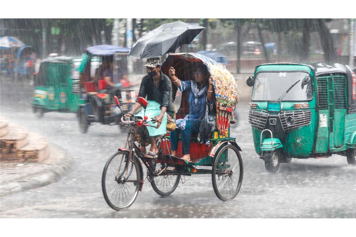 Menschen fahren im Monsunregen durch eine belebte Straße in Dhaka in Bangladesch.