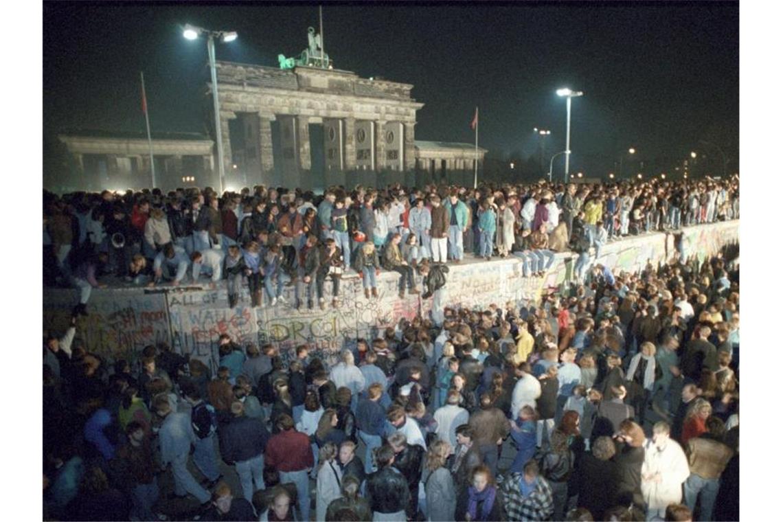 Menschen feiern auf der Berliner Mauer in der Nacht vom 9. auf den 10. November 1989. Foto: Peter Kneffel/dpa