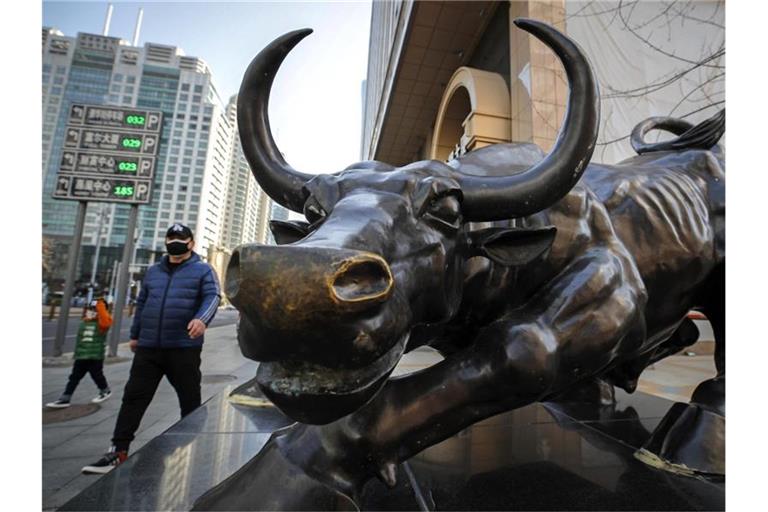 Menschen gehen an der Stier-Statue vor einem Bürogebäude in Peking vorbei. (Archivbild). Foto: Andy Wong/AP/dpa