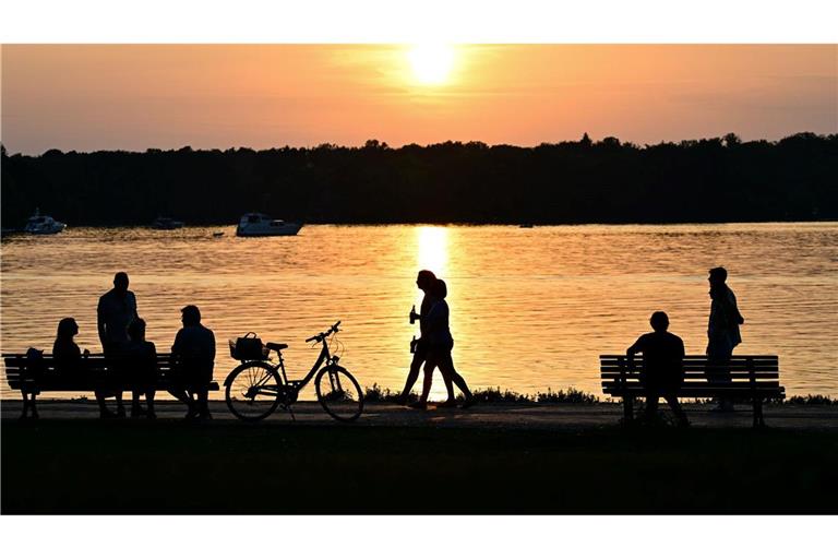 Menschen gehen bei Sonnenuntergang am Ufer des Tegeler Sees in Berlin.