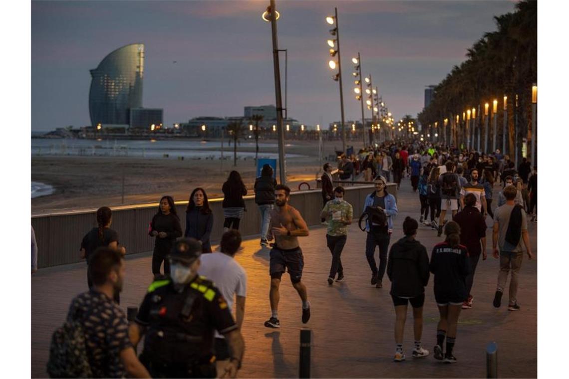 Menschen gehen bei Sonnenuntergang auf einer Strandpromenade spazieren und treiben Sport. Foto: Emilio Morenatti/AP/dpa