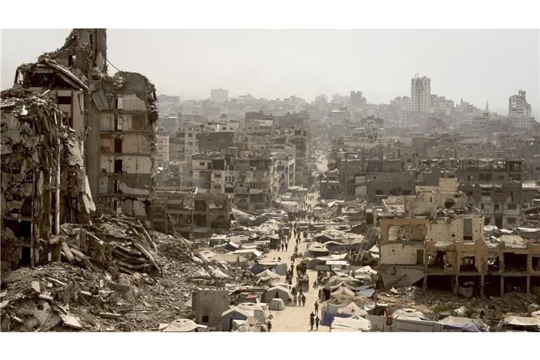 Menschen gehen eine Straße entlang, die von Gebäuden umgeben ist, die durch israelische Bombardierungen im Gazastreifen zerstört wurden.