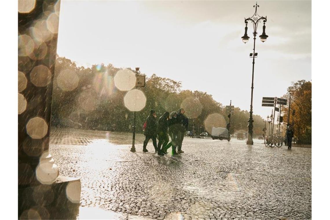 Menschen gehen in Sturm und Regen am Brandenburger Tor vorbei. Foto: Annette Riedl/dpa