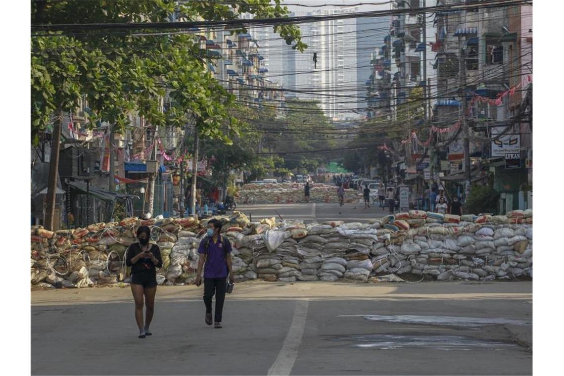 Menschen gehen in Yangon eine Straße entlang, auf der Demonstranten behelfsmäßige Barrikaden errichtet haben. Foto: ---/AP/dpa