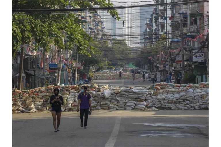Menschen gehen in Yangon eine Straße entlang, auf der Demonstranten behelfsmäßige Barrikaden errichtet haben. Foto: ---/AP/dpa