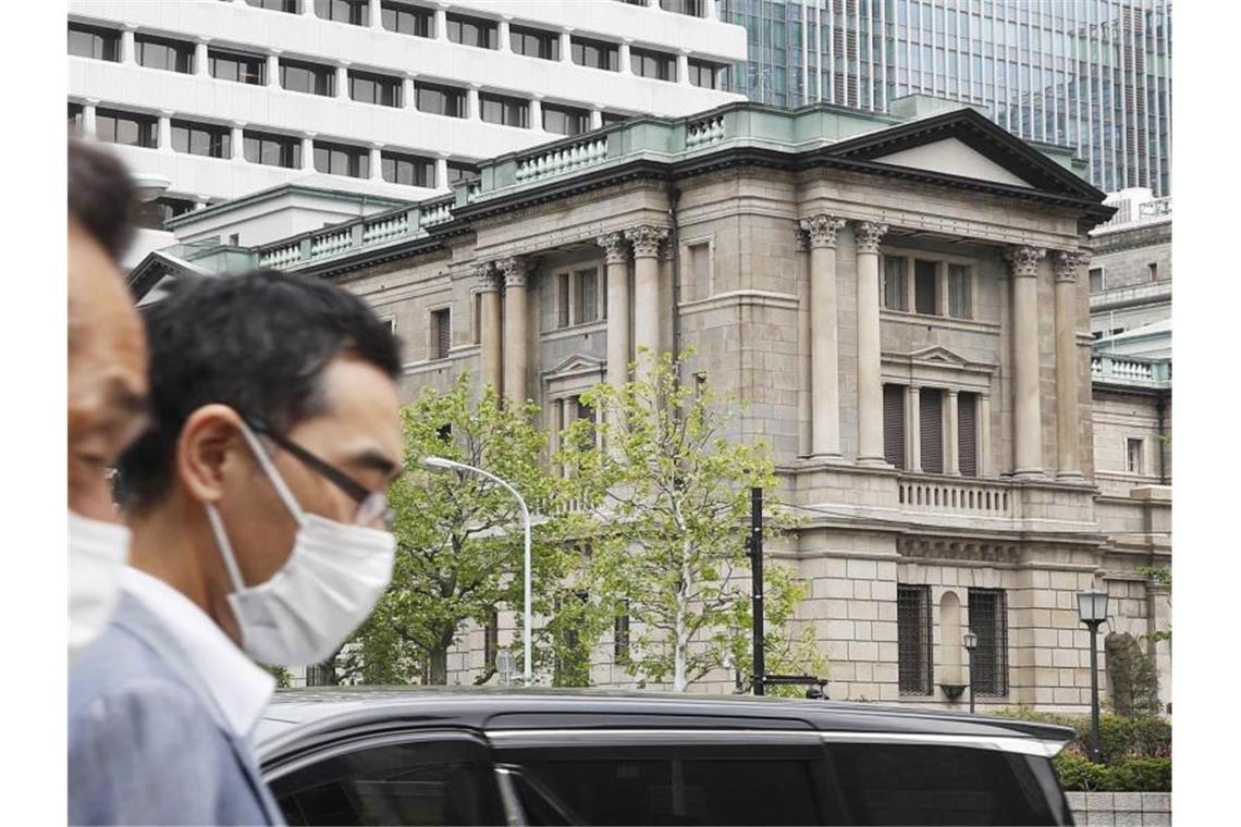 Menschen gehen mit Gesichtsmasken am Gebäude des Hauptsitzes der „Bank of Japan“ (BoJ) in Tokio vorbei. Foto: Shinji Kita/Kyodo News/AP/dpa