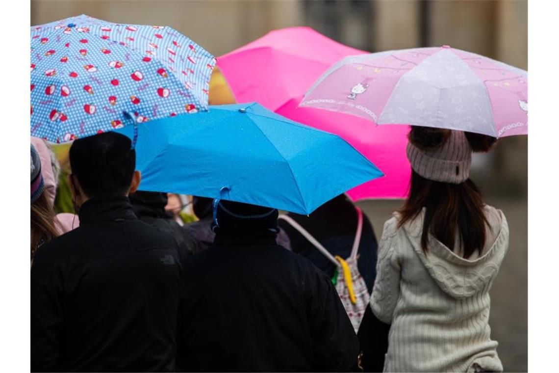 Menschen gehen mit Regenschirmen durch die Innenstadt. Foto: Robert Michael/dpa-Zentralbild/dpa/Symbolbild