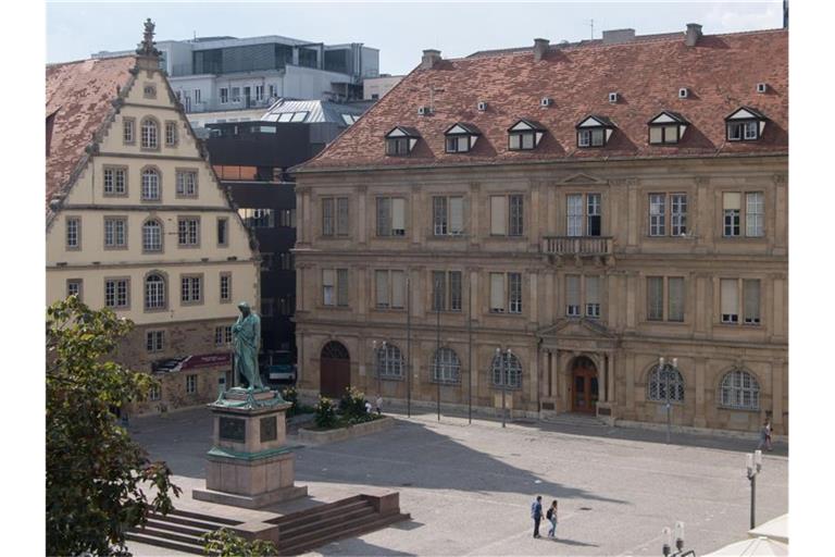 Menschen gehen über den Schillerplatz, auf dem der Stiftsfruchtkasten (l), das Schillerdenkmal (links unten) und das Justizministerium Baden-Württemberg (r) zu sehen sind. Foto: Marijan Murat/dpa/Archivbild